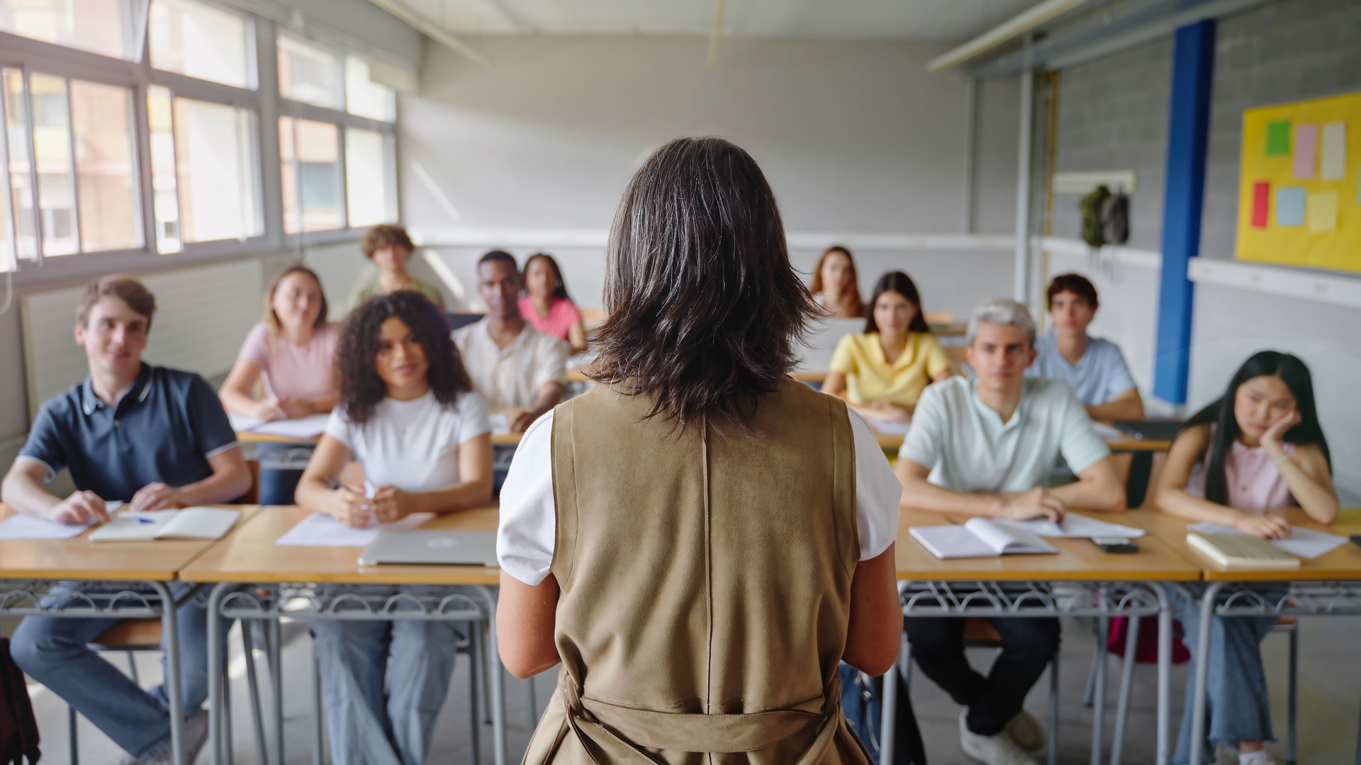 College students listening to mature woman teacher explaining lecture at High School