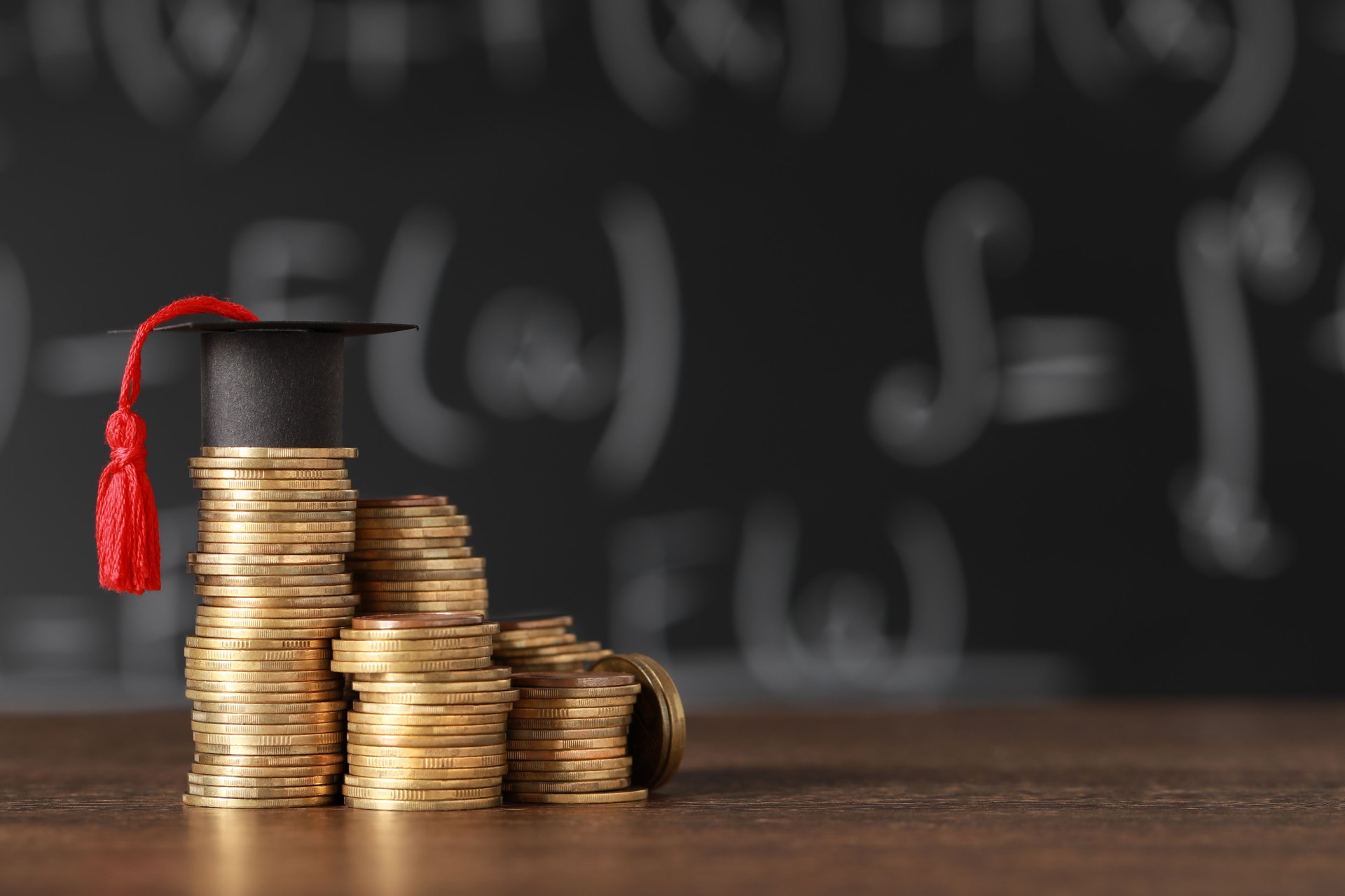 Scholarship concept. Coins and graduation cap on wooden table, space for text